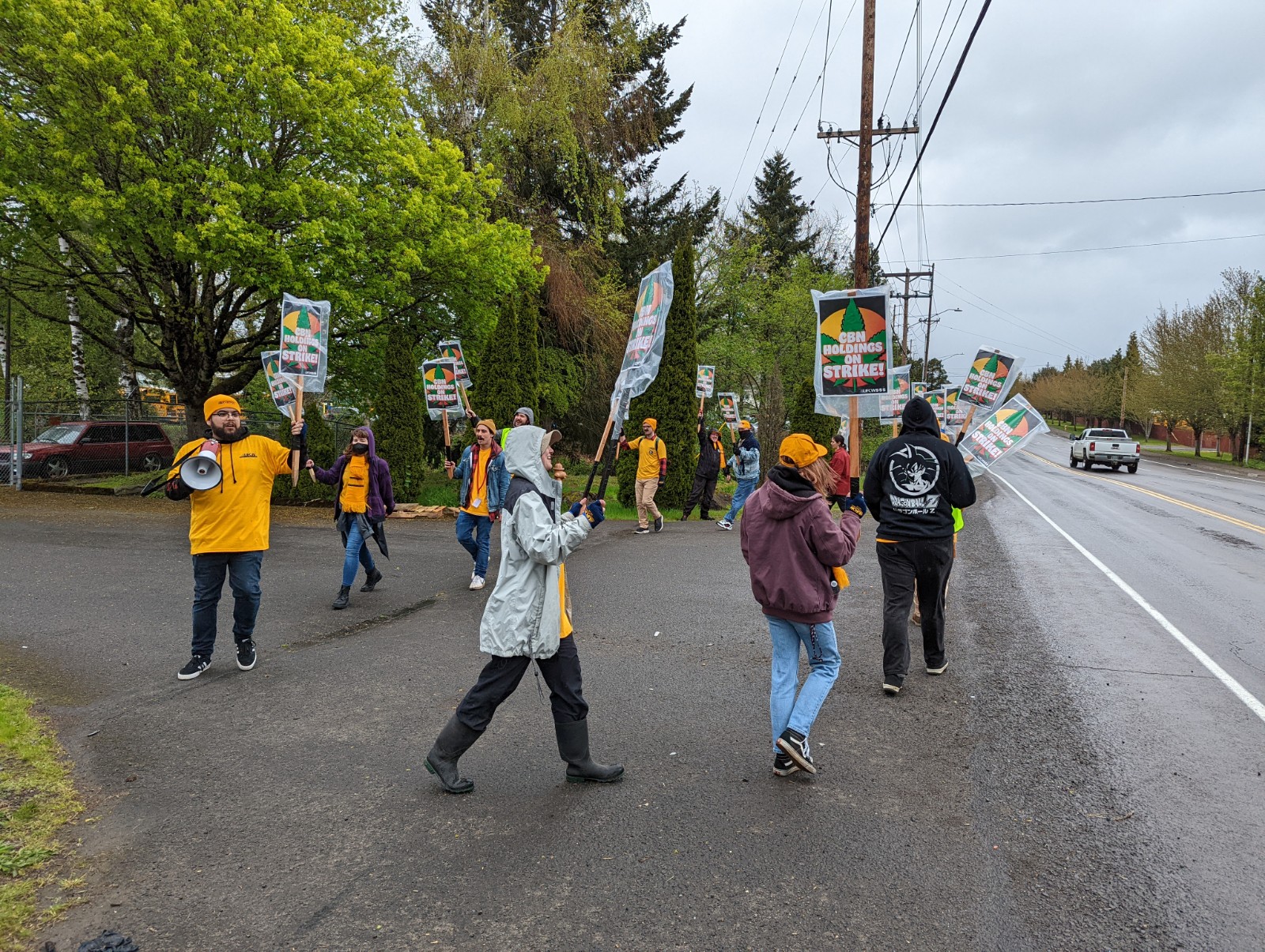 The strikers continue to circle in the driveway, holding their signs proudly. One of the strikers powerfully holds up a megaphone as they chant on the line.